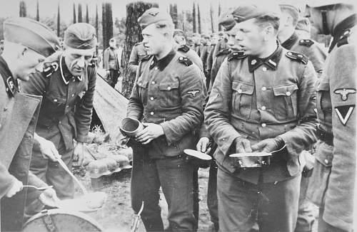 SS soldiers in chow line; camo helmets in background.