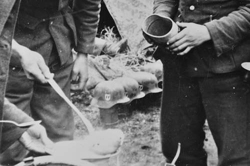 SS soldiers in chow line; camo helmets in background.